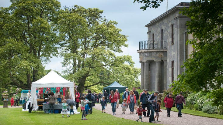 A fair on the lawn at Arlington Court, with smiling people and stalls set against the back drop of an impressive regency house.